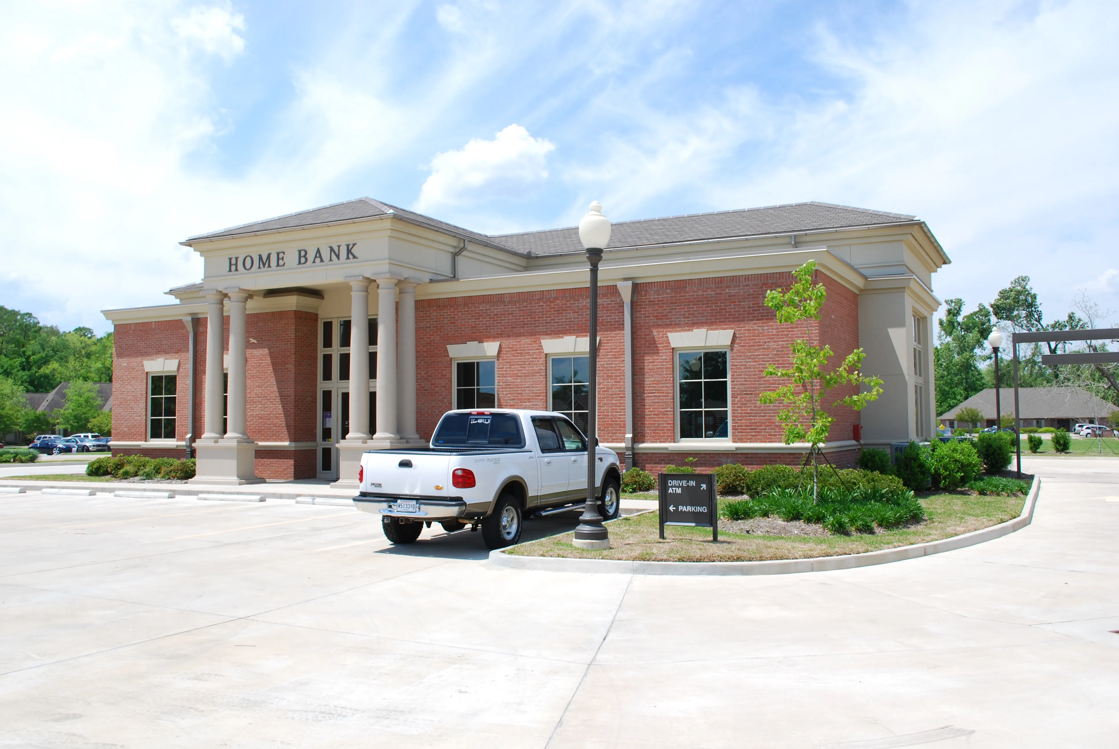 Angled view of the Home Bank branch showing the brick massing, hipped roof, and drive-in ATM signage.